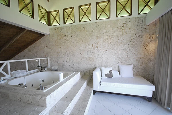 Suite de hotel con cama blanca, ba&ntilde;era y pared de piedra decorada