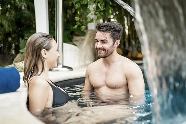 Pareja en una piscina exterior, hombre y mujer conversando sonrientes.