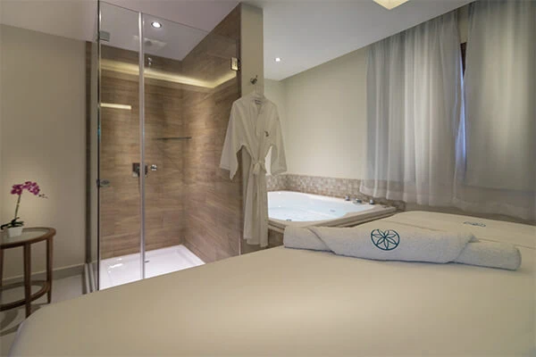 Ba&ntilde;o con ducha de vidrio, batas y jacuzzi en suite moderna.