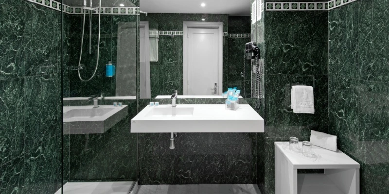 Ba&ntilde;o moderno con paredes verdes de m&aacute;rmol, lavabo y ducha.