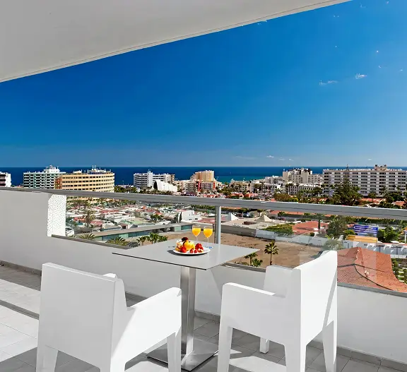 Terraza con mesa y sillas blancas, vista al mar y ciudad costera.