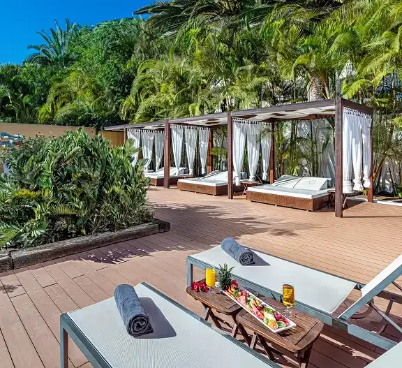 Terraza con camas y cortinas, rodeada de palmeras y vegetaci&oacute;n tropical