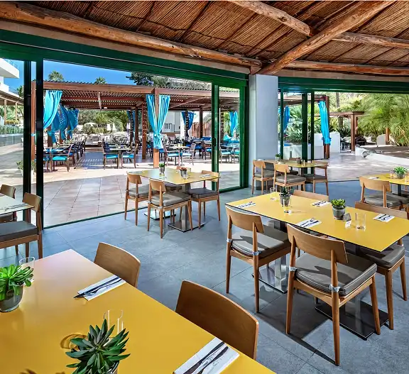 Comedor con mesas amarillas bajo techo de madera, sillas y sillas azules.