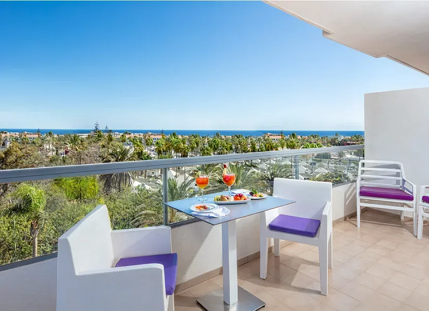 Terraza con mesa y copas, sillas moradas y vista al mar.