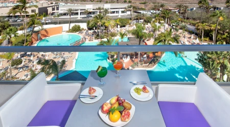 Vista de terraza con piscina y platos de frutas y ensaladas en mesa.