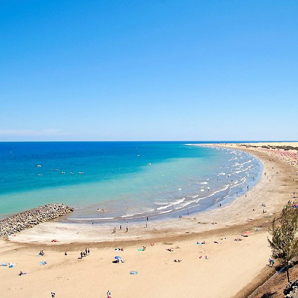 Playa de arena con olas y ba&ntilde;istas junto al mar, cielo despejado