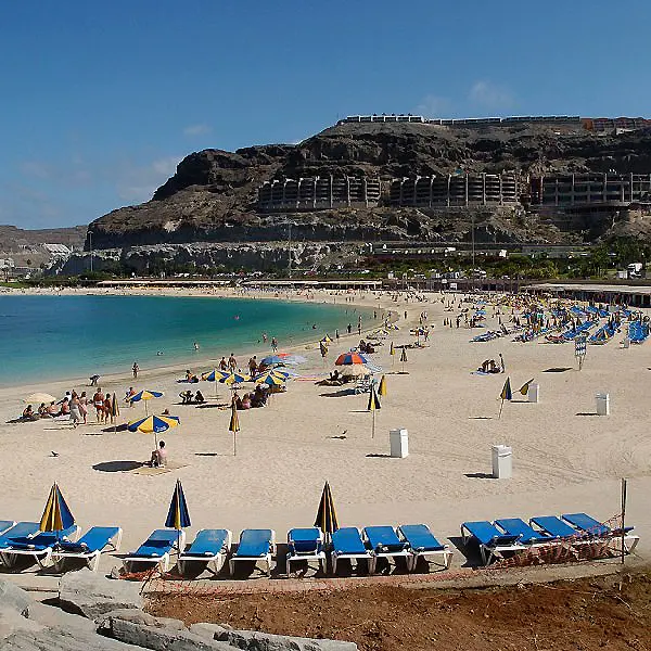 Playa con sombrillas y tumbonas frente a acantilado con hotel al fondo.