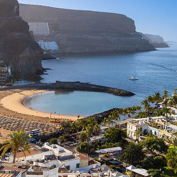 Playa de arena con aguas tranquilas, palmeras y acantilados al fondo