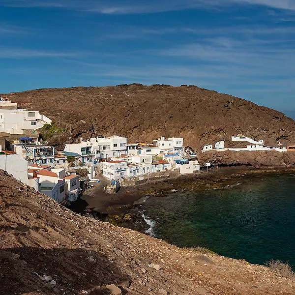 Pueblo costero blanco junto a una bah&iacute;a y monte rocoso al atardecer.