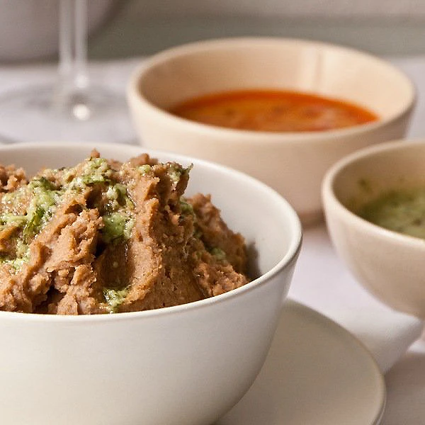 Cuencos con guiso desmenuzado y salsas en mesa blanca.