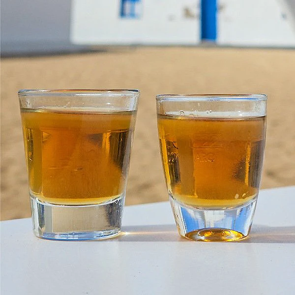 Dos vasos con l&iacute;quido &aacute;mbar sobre una mesa, en primer plano