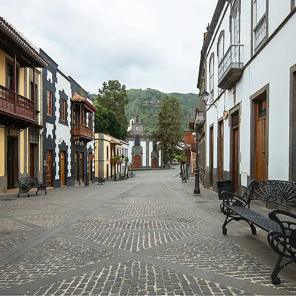 Calle empedrada con bancos y casas hist&oacute;ricas, al fondo una iglesia blanca