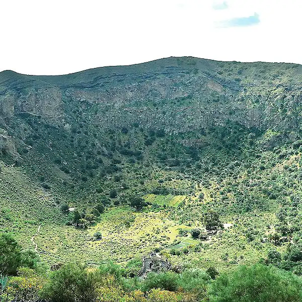 Ladera verde y monta&ntilde;as boscosas bajo cielo nublado