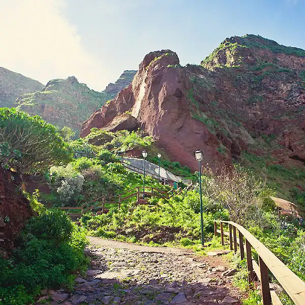 Sendero con valla y rocas monta&ntilde;osas verdes bajo cielo azul