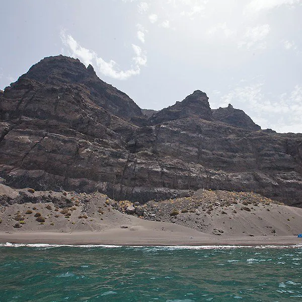 Monta&ntilde;as rocosas y playa con olas, vista del mar bajo el cielo nublado