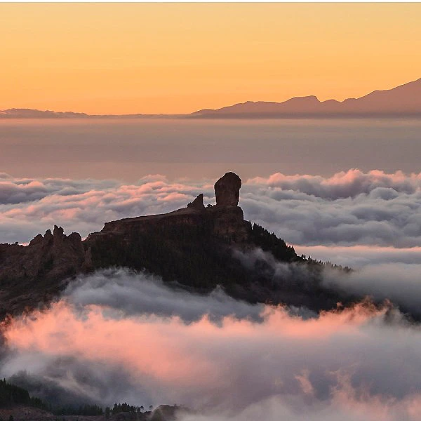 Monta&ntilde;a rocosa con una figura, sobre un mar de nubes al atardecer
