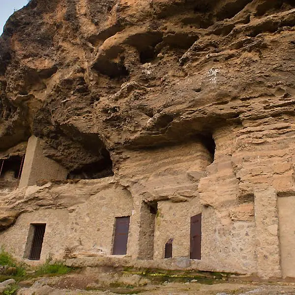 Ruinas de piedra en una pared rocosa con aberturas y ventanas.