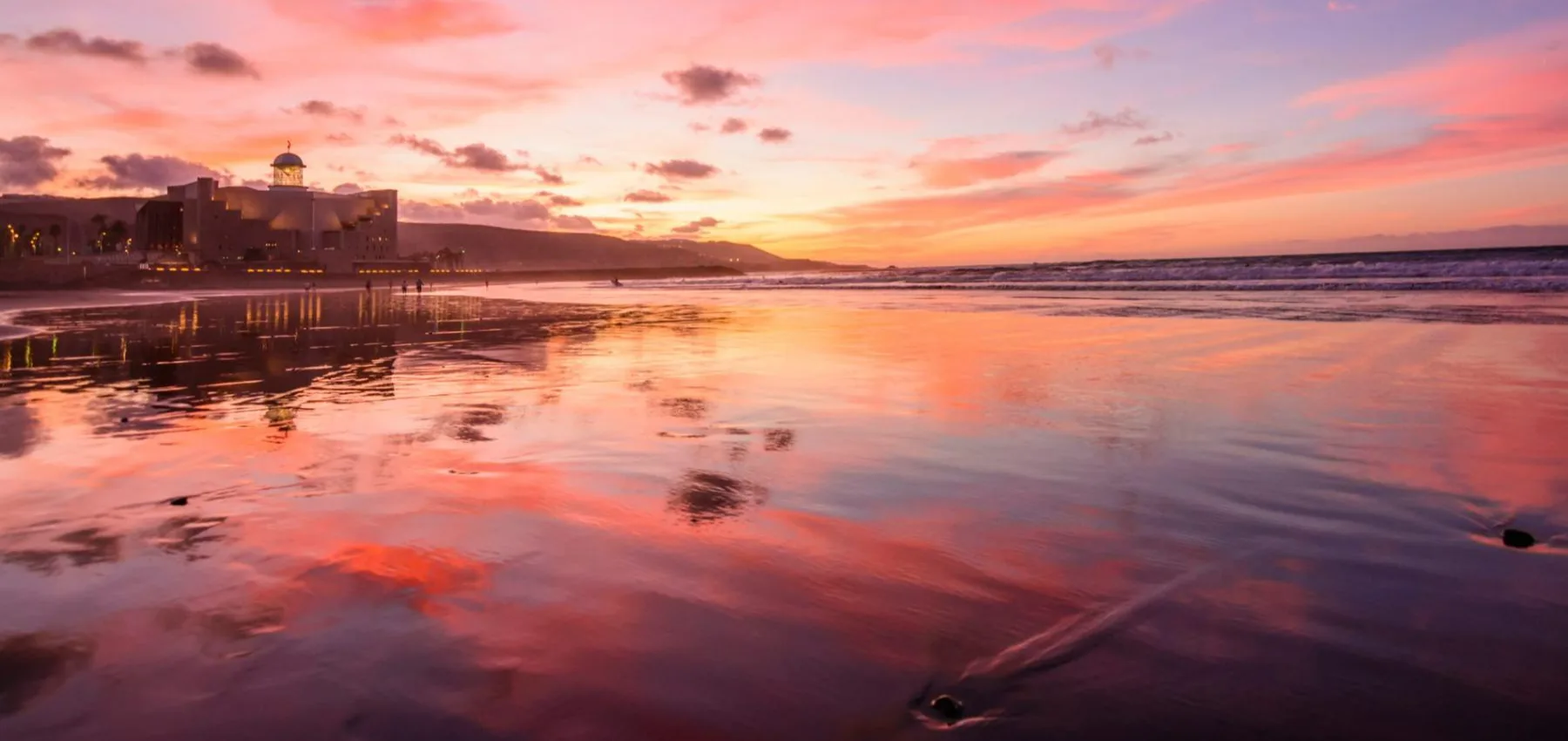 Atardecer en la costa con un edificio y reflejos en el agua