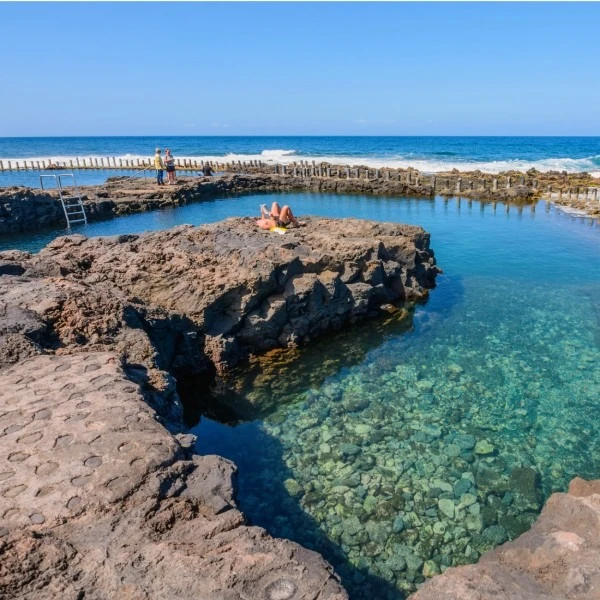 Piscina natural de mar con persona tomando el sol junto al muelle.