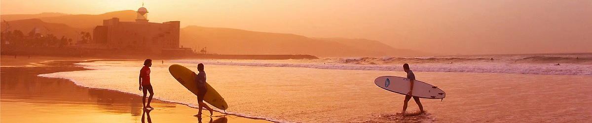 Tres surfistas en la playa al atardecer, con tablas en la orilla.