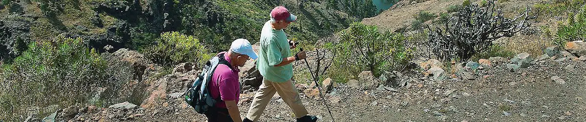 Senderistas caminando por un camino de monta&ntilde;a con bastones en la ladera.