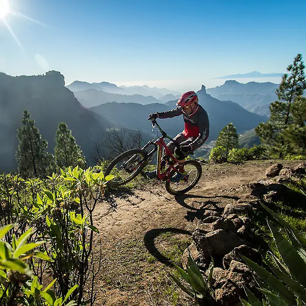 Ciclista de monta&ntilde;a con bicicleta roja en sendero entre rocas y valles.
