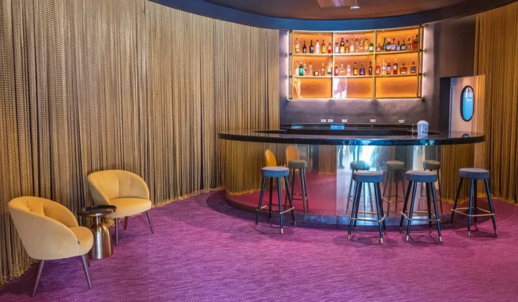 Bar con mostrador circular, taburetes y estanter&iacute;a con botellas iluminadas.