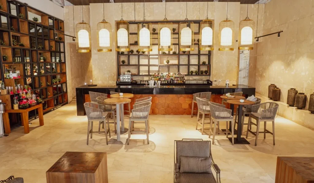 Bar acogedor con mesas de madera, sillas de rat&aacute;n y l&aacute;mparas colgantes.