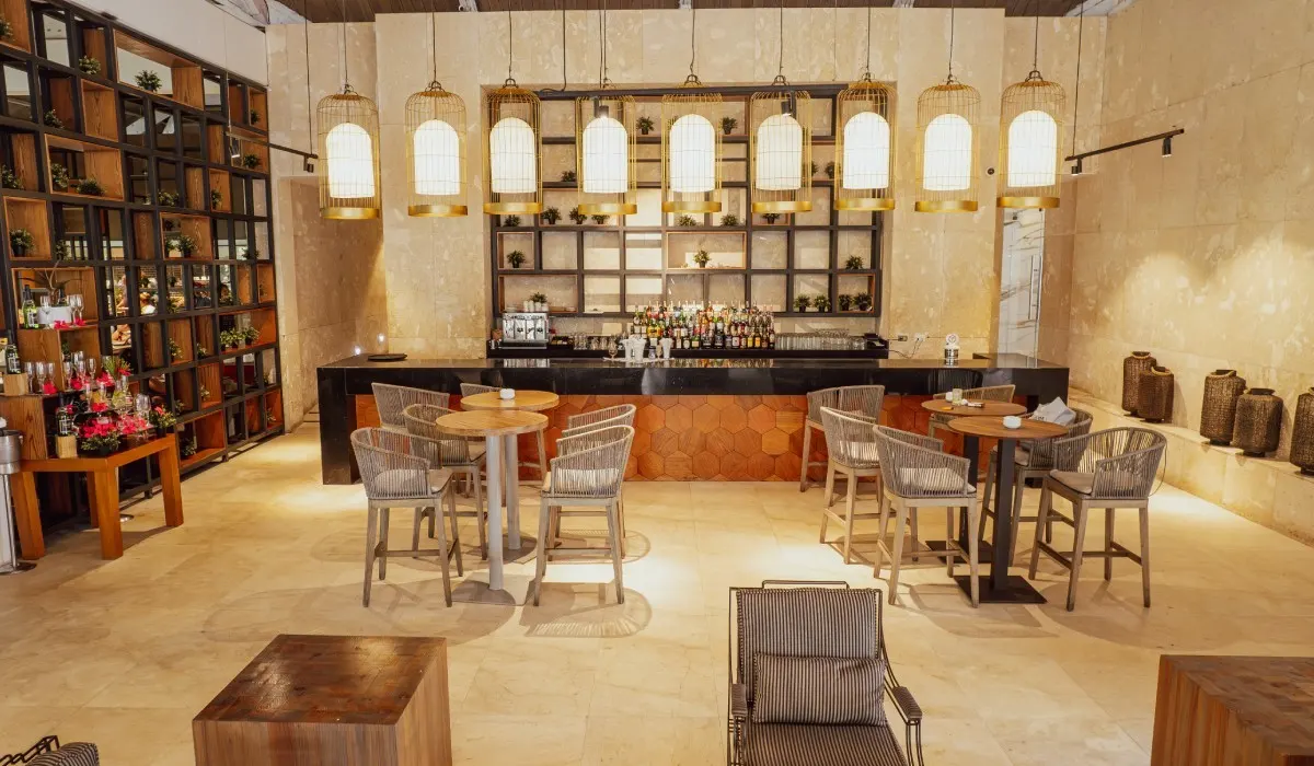 Bar acogedor con mesas de madera, sillas de rat&aacute;n y l&aacute;mparas colgantes.