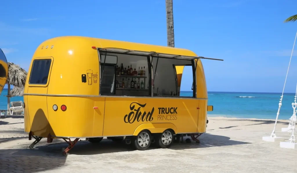 Caravana amarilla tipo truck con barra de bebidas junto al mar.
