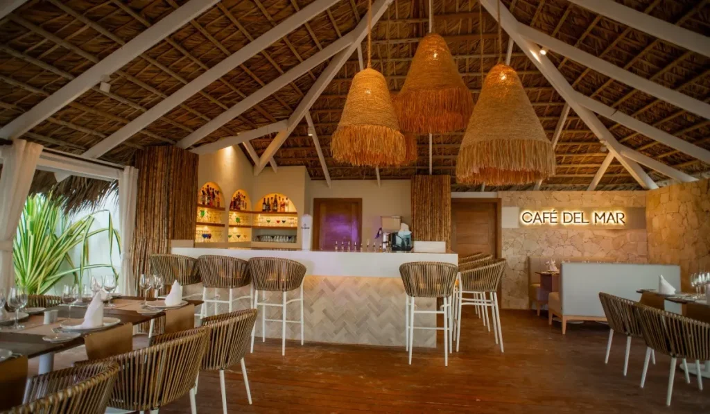 Interior de cafeter&iacute;a con barra, l&aacute;mparas de rafia y mesas bajo techo de palapa