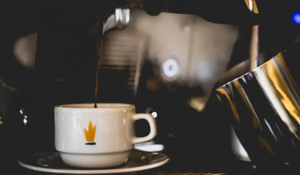 Taza de caf&eacute; sobre mesa, fondo oscuro con luz y una cafetera de metal
