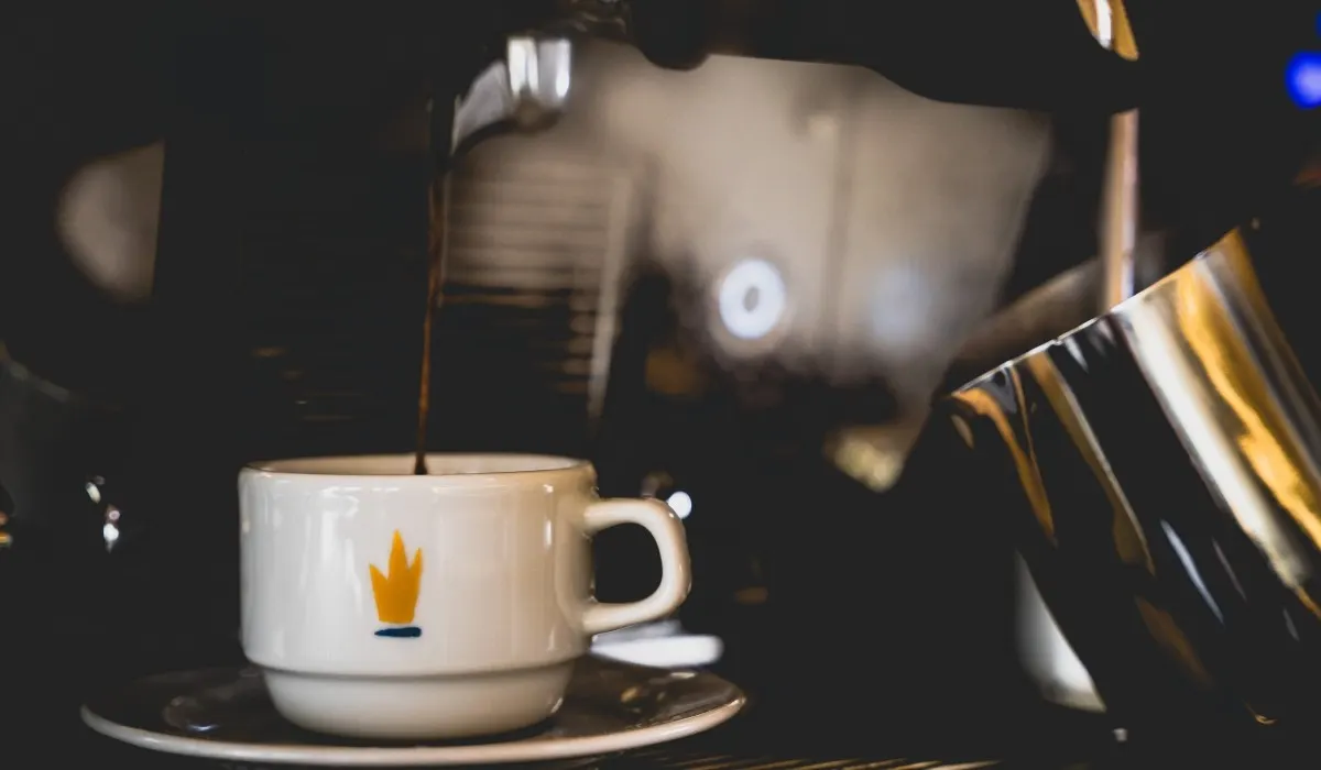 Taza de caf&eacute; sobre mesa, fondo oscuro con luz y una cafetera de metal
