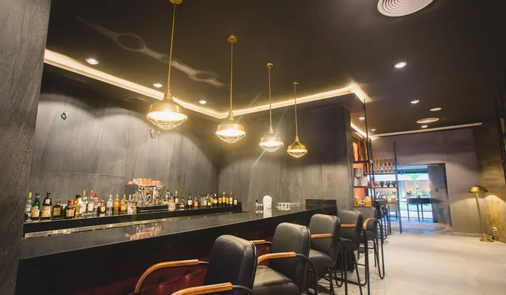 Bar con bebidas, barra negra y sillas de cuero, iluminaci&oacute;n colgante.