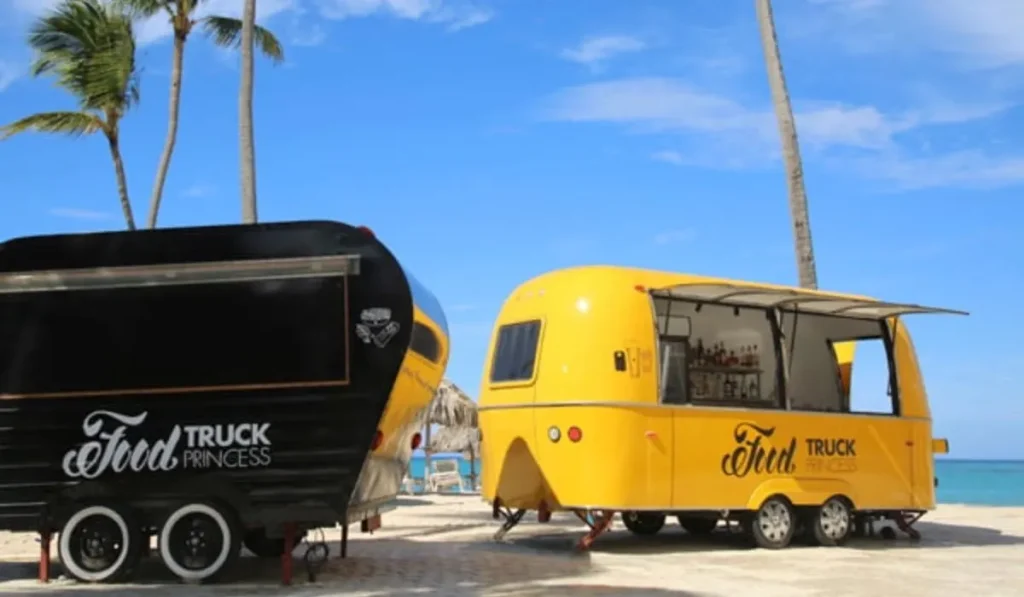 Cami&oacute;n vintage y food truck amarillo frente al mar con palmeras al fondo