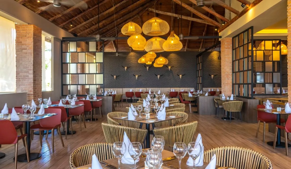 Comedor elegante con mesas servidas y l&aacute;mparas colgantes de mimbre en techo de vigas
