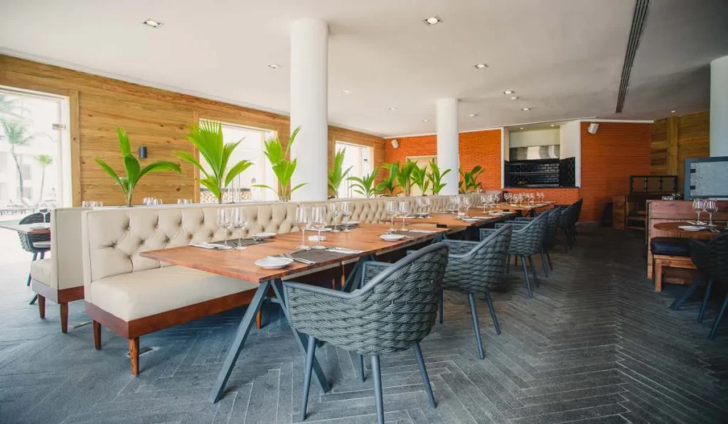 Comedor moderno con mesas, sillas y plantas, en un espacio de madera y ladrillo