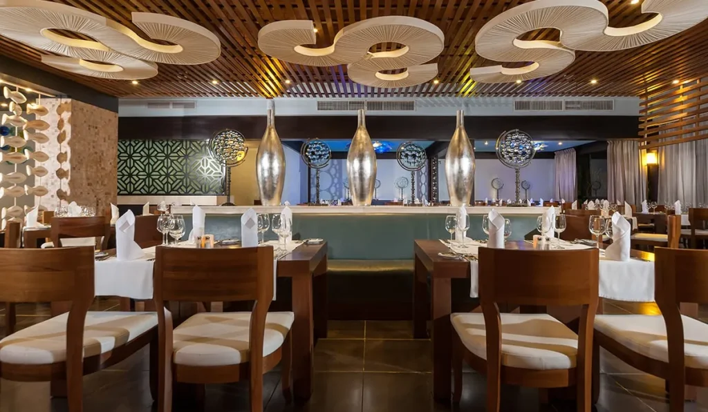 Restaurante elegante con mesas, sillas blancas y l&aacute;mparas circulares sobre la barra