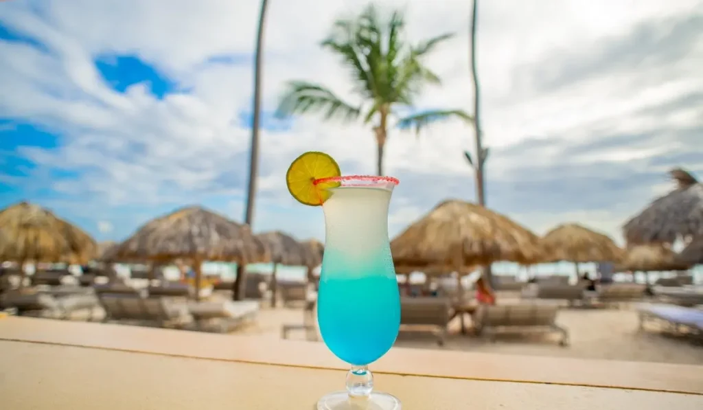 C&oacute;ctel azul con rodaja de lim&oacute;n en bar de playa con sombrillas al fondo