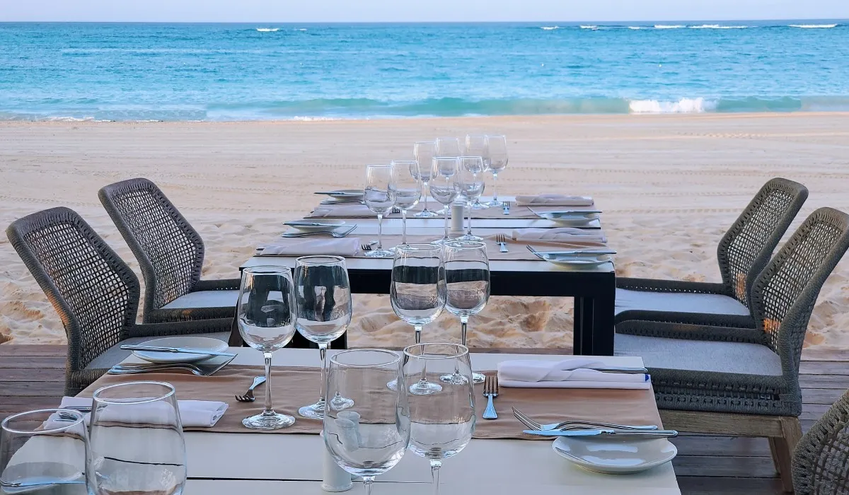 Mesa servida en la playa, junto al mar con copas y vajilla al atardecer