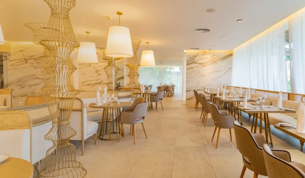 Sal&oacute;n luminoso con mesas y sillas, l&aacute;mparas colgantes y decoraci&oacute;n elegante.
