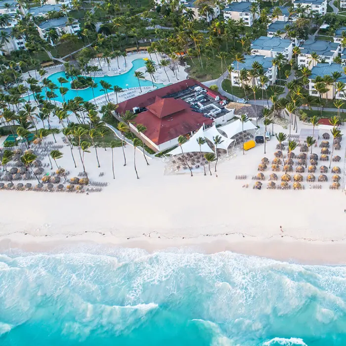 Vista a&eacute;rea de un hotel junto a la playa, piscina y palmeras.