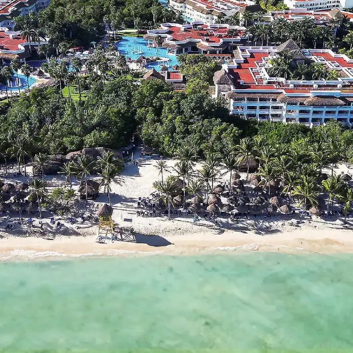 Vista a&eacute;rea de un hotel junto a la playa, con piscinas y palmeras.