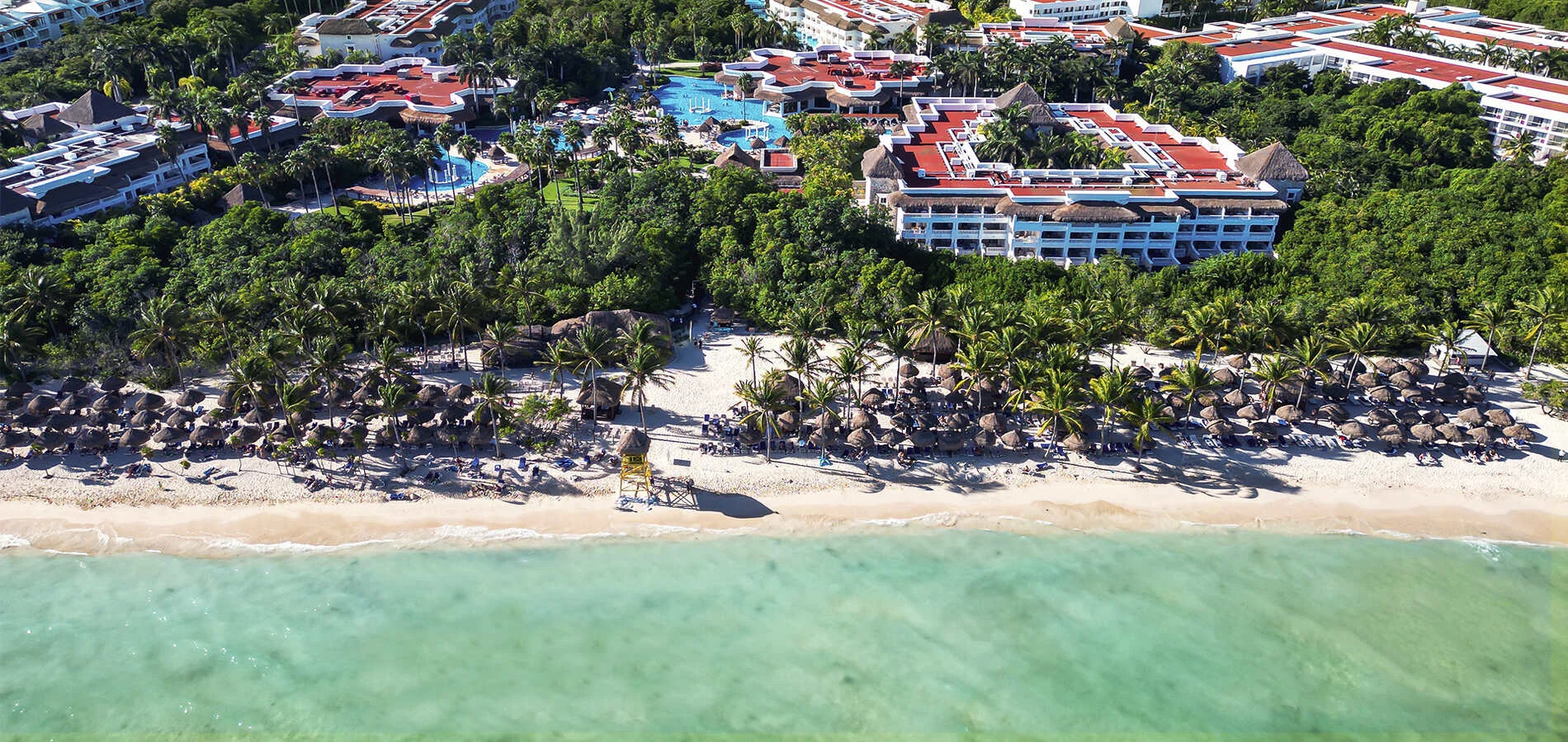 Vista a&eacute;rea de un hotel junto a la playa con palmeras y piscinas en marea verde