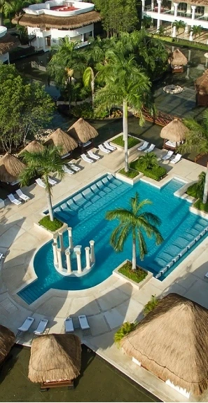 Piscina azul con palmeras y caba&ntilde;as r&uacute;sticas en un hotel tropical.