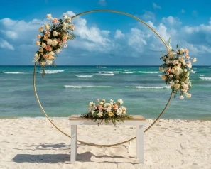 Arco floral sobre pedestal en una playa con olas y cielo azul