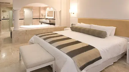 Habitaci&oacute;n moderna con cama doble, cojines y luz c&aacute;lida.