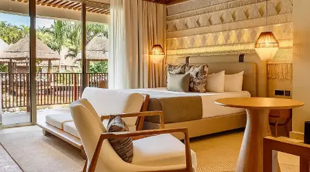 Habitaci&oacute;n hotelera con cama, sill&oacute;n, l&aacute;mparas y terraza con vista al jard&iacute;n
