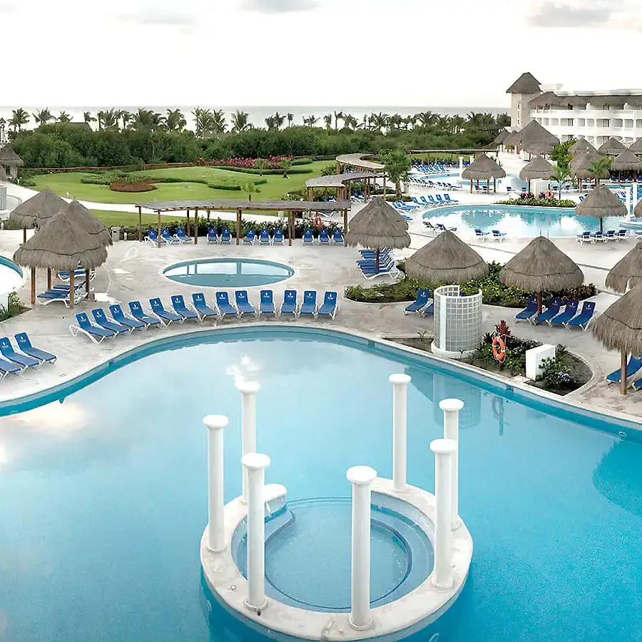 Piscina de hotel con tumbonas azules y caba&ntilde;as de palma al fondo
