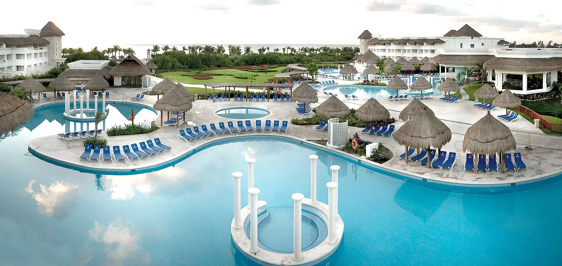 Piscina azul con camastros y caba&ntilde;as de paja en complejo tur&iacute;stico tropical